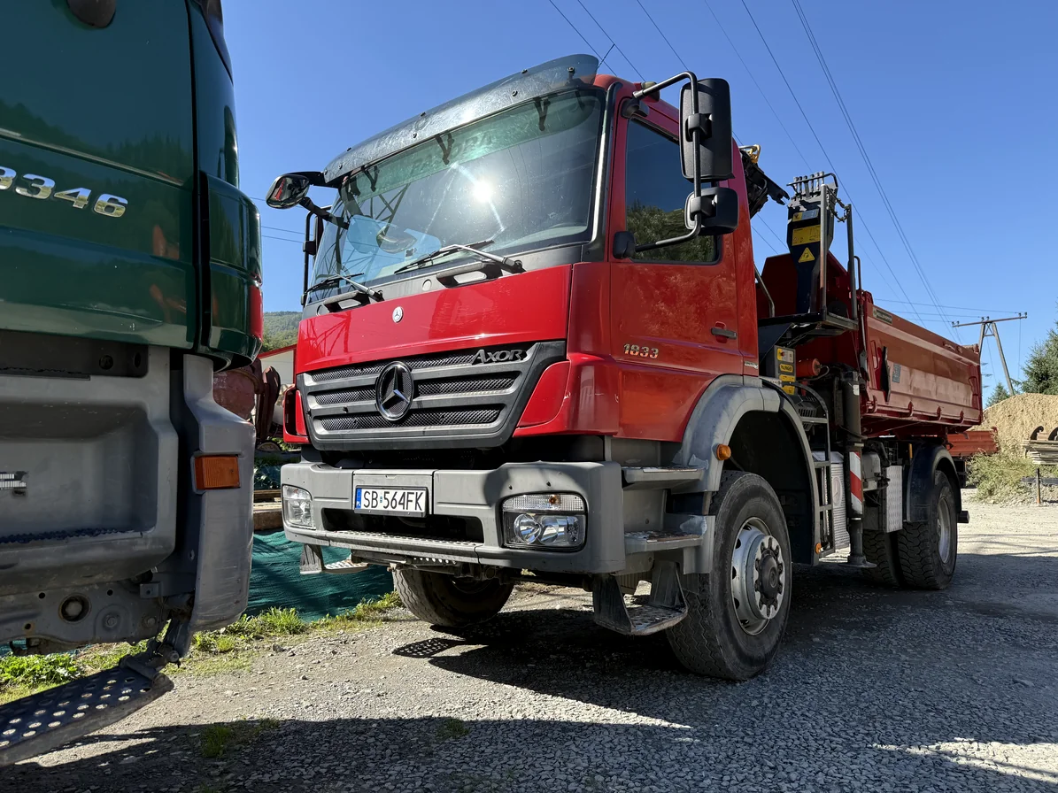Czerwona wywrotka Mercedes Axor z żurawiem HDS na placu firmowym.